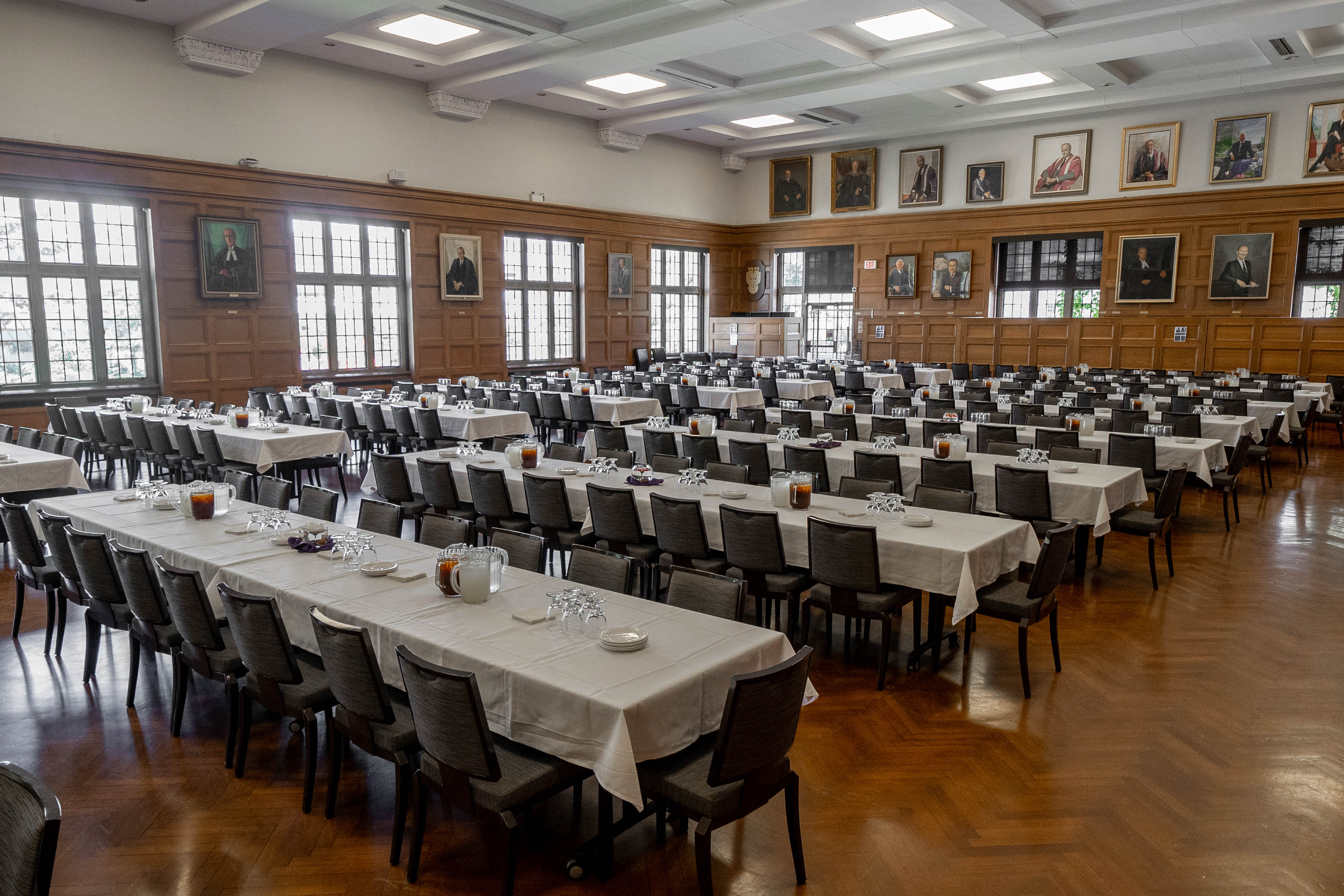 Great Hall in Somerville House set up for an event with long banquet tables covered in white cloths, gray chairs, and wood-paneled walls decorated with framed portraits.